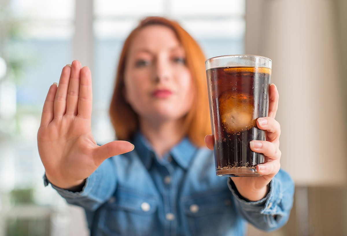foods to avoid for healthy teeth woman holding her hand out to stop you from drinking a glass of soda foods to avoid for healthy teeth